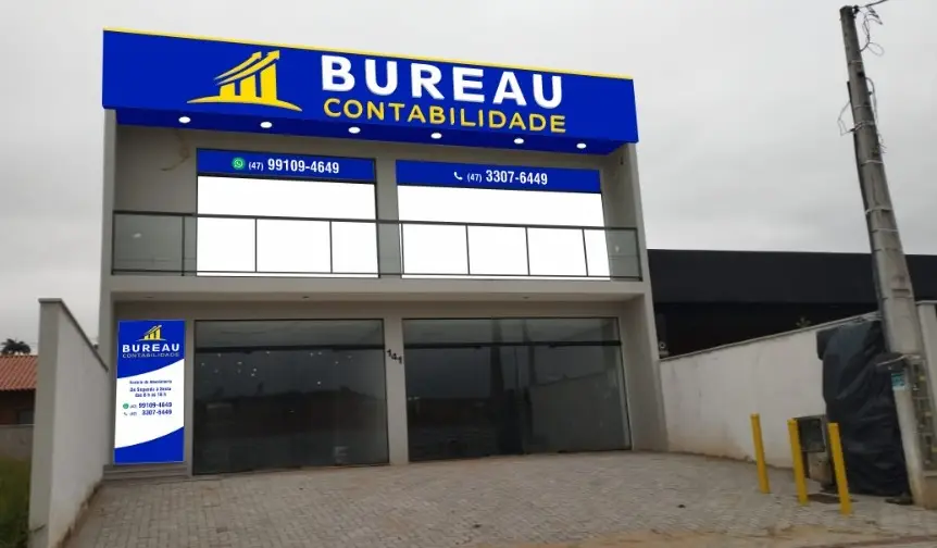Fachada do escritório da Bureau Contabilidade, prédio de dois andares com letreiro azul e amarelo e os telefones na vitrine