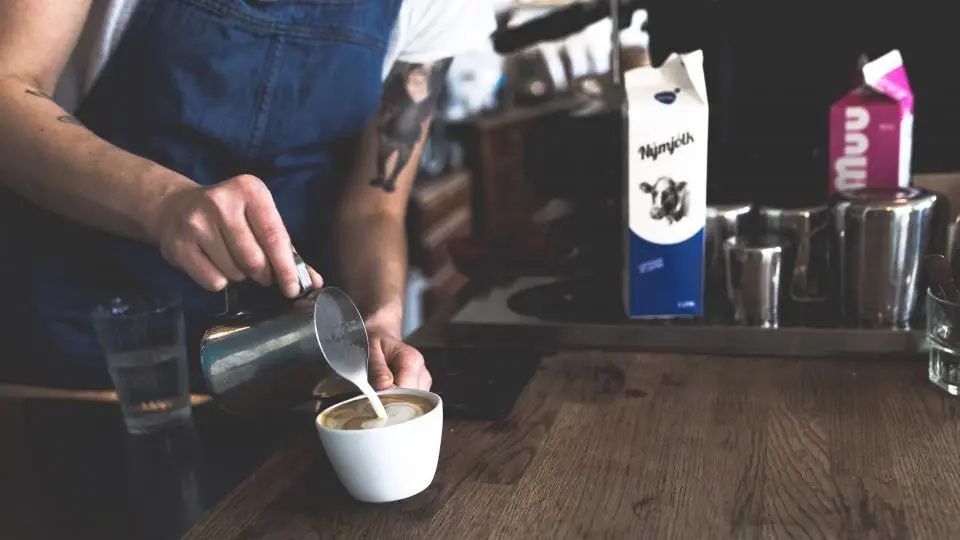 Barista despejando leite vaporizado em uma xícara de café