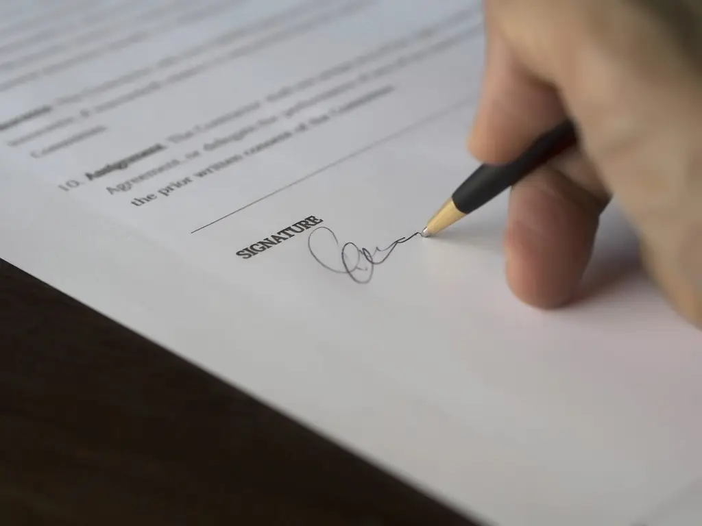 Mão assinando um contrato com caneta, em close na linha de assinatura
